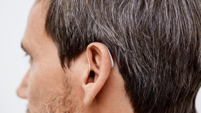 Das Ohr eines Mannes, welcher ein Hinter-dem-Ohr Hörgerät trägt